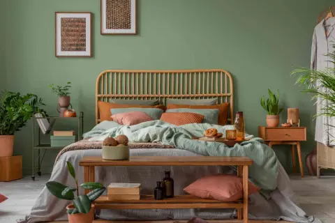 Gemütliches Schlafzimmer mit Rattan-Kopfteil, mintgrüner Bettwäsche und Korallen-Akzenten. Ein Holzbett mit Kissen und Decken lädt zum Entspannen ein. Pflanzen und Bilder runden das Ambiente ab, um das Bett perfekt einzurichten.