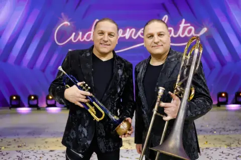 Dwóch muzyków z orkiestry Golec trzyma instrumenty: jeden trąbkę, drugi puzon.