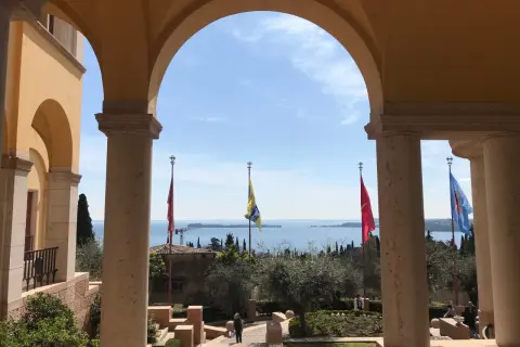 Arco con vista sul lago, giardini e bandiere che sventolano, ricordando l'atmosfera della villa d'Annunzio.