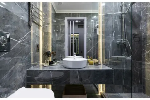 Une **salle de bain de rêve** aux murs de marbre gris, avec vasque ronde, douche moderne et éclairage d'ambiance.