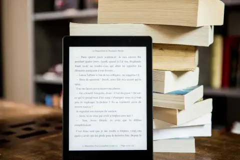 Liseuse affichant un roman, à côté d'une pile de livres. Idéal pour trouver un epub gratuit sans inscription et plonger dans une nouvelle histoire.