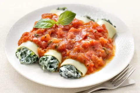 Cannelloni ricotta épinard généreusement nappés de sauce tomate, garni d'une feuille de basilic. Un plat savoureux et réconfortant.