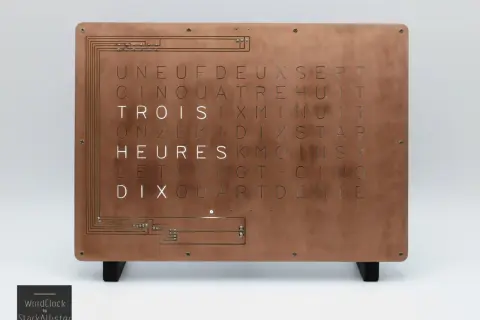 Horloge murale au design industriel, avec une plaque de cuivre gravée de lettres formant des mots. Une lettre métal unique pour un style épuré.