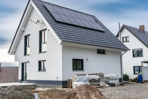 Nowy dom z panelami słonecznymi na dachu, w trakcie rozbudowy. Wokół materiały budowlane.