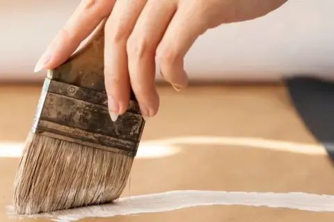 Main d'une personne peignant une surface en MDF avec un pinceau blanc.