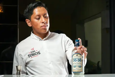 Młody mężczyzna w białej koszuli prezentuje butelkę tequili 30-30 Reserva Especial Blanco, podkreślając, z czego jest tequila – ze 100% niebieskiej agawy.