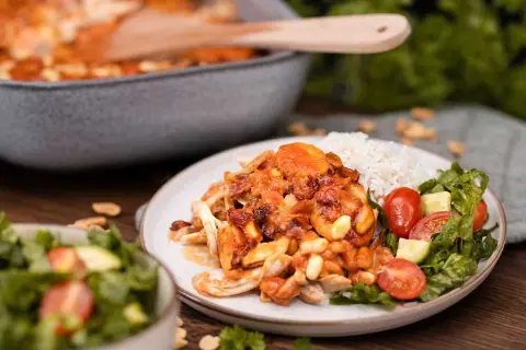 En tallrik med flygande jakob originalrecept, ris och sallad. Kycklingen är täckt av en krämig sås med jordnötter och bacon.