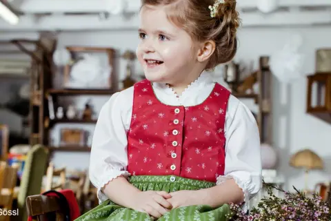 Ein fröhliches Mädchen im Dirndl mit einer hübschen Schleife im Haar. Die Tracht ist für Kinder perfekt.