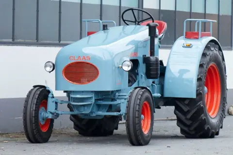Niebieski ciągnik jednoosiowy Claas Jumbo z pomarańczowymi felgami i grillem.