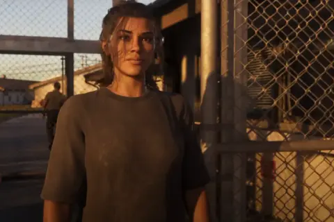 Lucia z GTA 6 stoi przed bramą, za nią widać budynki i strażnika.