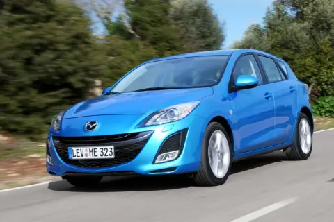 Niebieska Mazda 3 2010 w wersji hatchback pędzi po krętej drodze wśród zieleni.