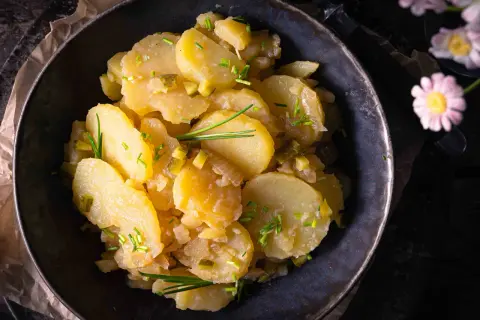 Schüssel mit Kartoffelsalat ohne Mayo, garniert mit Schnittlauch und Gurkenstückchen.