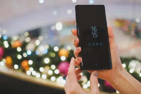 Ręce trzymające czarny smartfon Samsung, na ekranie zegar i ikony. Planowane zgranie kontaktów z Samsunga na komputer.