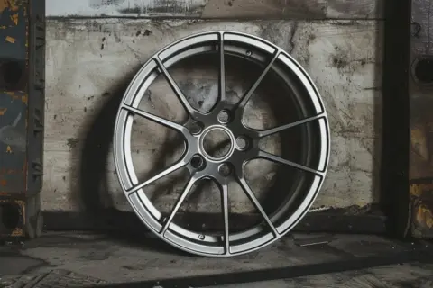Nowoczesna felga aluminiowa 16 cali, z wieloma ramionami, prezentuje się na tle industrialnej ściany.