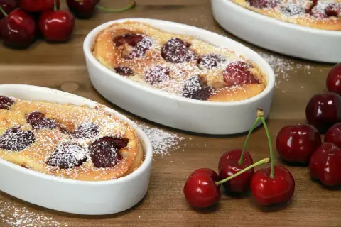 Deux clafoutis sans oeuf aux cerises, saupoudrés de sucre glace, sur une table en bois. Des cerises fraîches sont disposées autour.