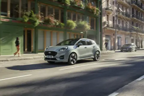 Jasnoszary Ford Puma jedzie ulicą miasta. Sprawdź aktualną ford puma cena i możliwości tego stylowego SUV-a.
