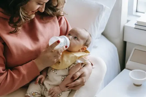 Mama karmi butelką dziecko, które ma problem z brakiem pokarmu po porodzie.
