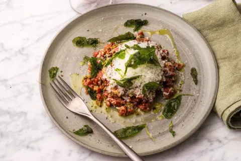 En tallrik med läcker carne cruda, toppad med riven ost och färska örter, redo att avnjutas med en gaffel.