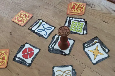 Karty gry Jungle Speed rozłożone na podłodze, gotowe do szybkiej rozgrywki. Drewniany totem pośrodku.