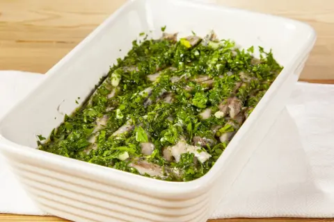 Acciughe al verde in una teglia bianca, condite con abbondante prezzemolo tritato e aglio.