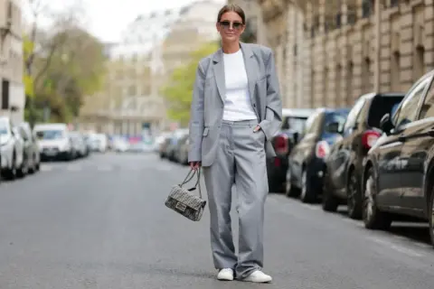 Elegancka stylizacja smart casual damski lato: szary garnitur, biały top, sneakersy i torebka Fendi.