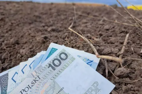 Pieniądze leżą na ziemi, symbolizując trud rolnika i jego ubezpieczenie społeczne.