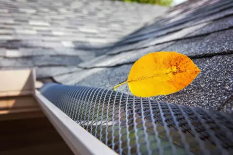 A yellow leaf rests on a newly installed gutter guard, showcasing its effectiveness against falling debris.