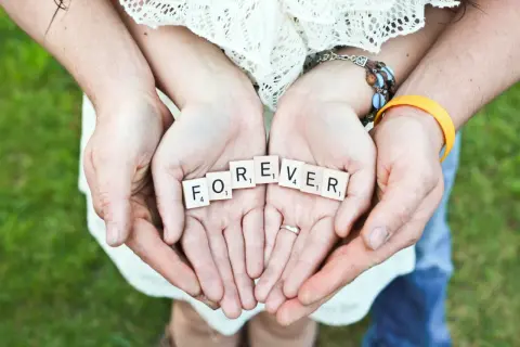 Hände halten Scrabble-Steine mit "FOREVER". Ein Paar feiert seinen 42. Hochzeitstag.