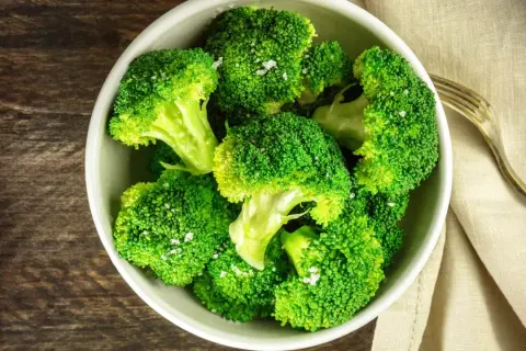 En skål med nykokt, grön broccoli, strödd med flingsalt. En gaffel ligger bredvid på en beige duk.