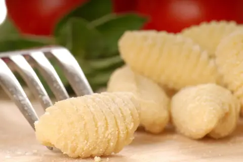 Une fourchette pique un gnocchi fait maison, prêt pour une délicieuse recette gnocchi. Des gnocchis frais et des ingrédients italiens en arrière-plan.