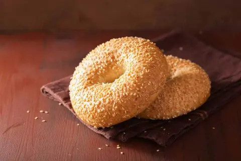 Deux bagels dorés, recouverts de graines de sésame, sur une serviette brune. Parfait pour une recette bagel moelleux.