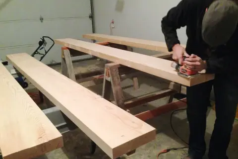 Man sanding Douglas fir planks on sawhorses, preparing them for staining.