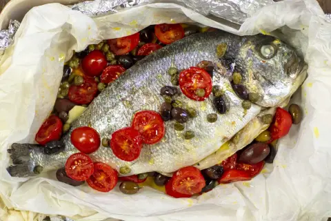 Orata al cartoccio con pomodorini, olive e capperi, cotta in forno.
