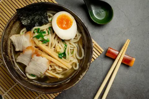 Miseczka aromatycznego ramenu z plastrami wieprzowiny, jajkiem na pół, bambusem i nori. Idealny przepis, jak ugotować ramen.