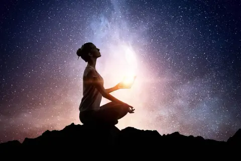 Silueta de mujer meditando bajo un cielo estrellado, sosteniendo una luz brillante. Conexión cuantica espiritual.
