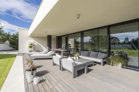 Terraza moderna con muebles grises y una puerta corredera elevable o osciloparalela que da a un jardín verde.