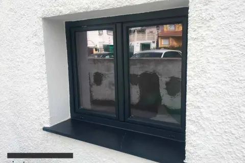 Ventana con marco oscuro y un alféizar negro que funciona como vierteaguas, protegiendo la pared de la lluvia.