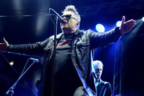 Wokalista zespołu T.Love w skórzanej kurtce śpiewa do mikrofonu, z rękami rozłożonymi szeroko.