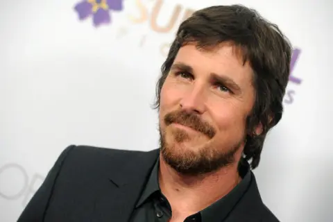 Christian Bale z brodą i w garniturze, znany z wielu świetnych christian bale filmów.