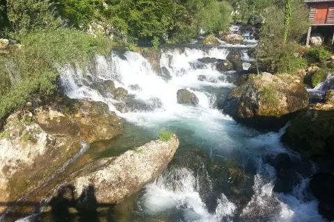 Vattenfall och klippor vid en flod nära Banja Luka. En liten röd stuga skymtar bland träden.
