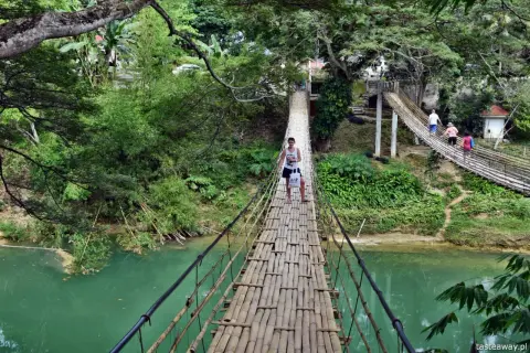 Młody mężczyzna idzie przez bambusowy most wiszący nad turkusową rzeką na Bohol, Filipiny.