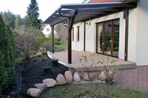 Terrasse sanieren: Neue Holzterrasse mit Überdachung, daneben frisch aufgeschüttete Erde und Steine für die Gartengestaltung.