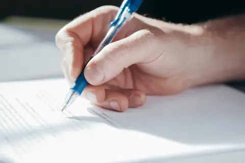 Dłoń pisze długopisem na dokumencie, który może być pełnomocnictwem do zarządzania nieruchomością.