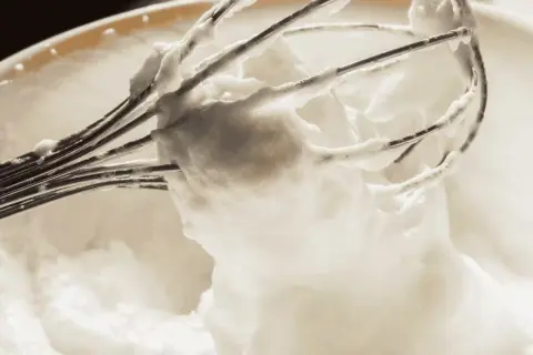 Fouet de cuisine couvert de mousse blanc en neige, prêt pour une pâtisserie légère et aérienne.