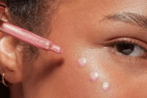 Applicazione di illuminante liquido sul viso con contagocce per un look radioso.