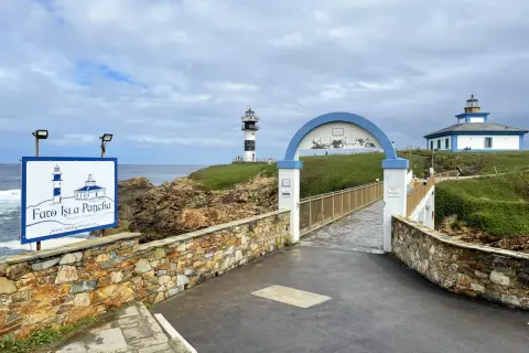 El faro de Ribadeo, con su icónico diseño blanco y negro, se alza sobre un acantilado verde. Un puente arqueado conduce a la isla.