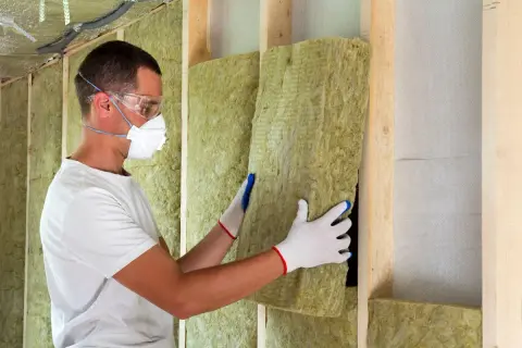 Operaio con mascherina e occhiali installa pannelli di lana di roccia per un cappotto termoisolante.
