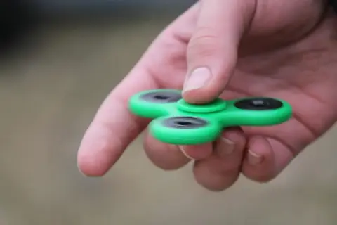 Groene fidget spinner in hand, een hulpmiddel voor concentratie bij hoog functionerend autisme.