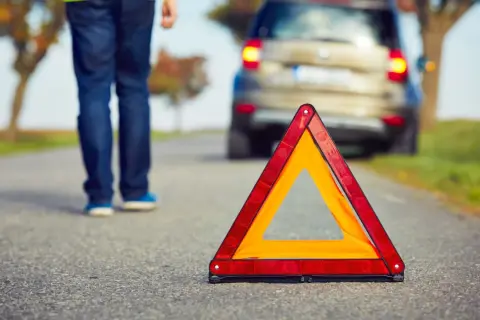 Triángulo de emergencia en carretera. Persona se aleja de coche averiado, lista para proteger, alertar y socorrer.