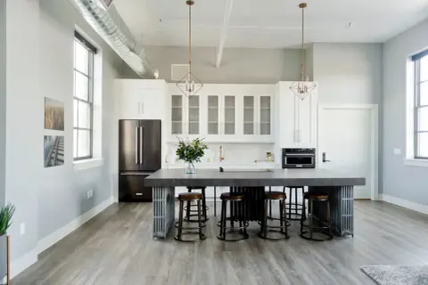 Cuisine moderne avec îlot central, tabourets et armoires blanches. Une cuisine sans hotte, avec un style épuré et industriel.